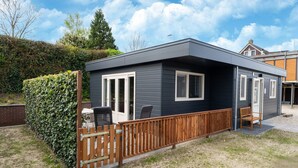 Ein modernes, eingeschossiges Haus mit dunkler Fassade, einer Holzterrasse und einer kleinen Patio.