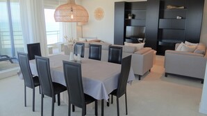 A modern living room with a dining area, featuring a large dining table, black chairs, a grey sofa, and a black entertainment unit with a TV. - Apartment in Nieuwpoort for 6 Persons (Nieuwpoort)