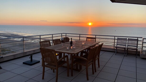 A terrace with a table and chairs facing the ocean at sunset. - Apartment in Nieuwpoort for 6 Persons (Nieuwpoort)