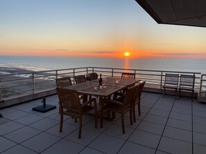 A terrace with a table and chairs facing the ocean at sunset. - Apartment in Nieuwpoort for 6 Persons (Nieuwpoort)