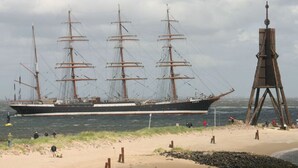Ein großes Segelschiff liegt an einem Strand, in der Nähe steht eine hohe Holzkonstruktion.