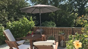 Eine Terrasse mit Holztisch und -stühlen, einem großen Sonnenschirm und Topfpflanzen.