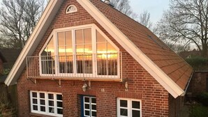 Ein zweigeschossiges Backsteinhaus mit einem Dachfenster, einer blauen Tür und einem Balkon mit Metallgeländern.