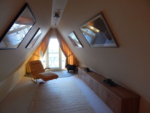 A narrow attic bedroom with a sloped ceiling, large windows, and a single bed.