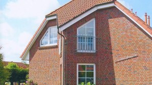 A two-story brick house with a sloped roof, a small front porch, and a visible front yard with a gate. - Strandraubernest Comfortable Holiday Residence (Dornum)