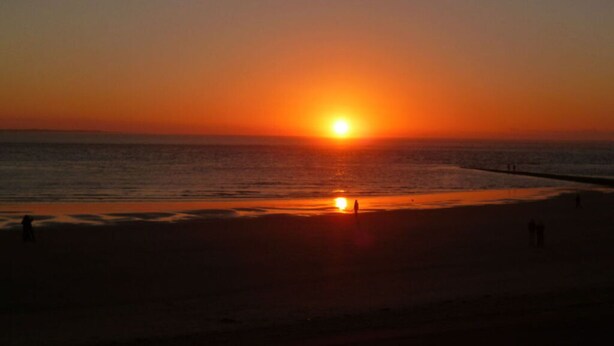 A sunset over a beach with a calm sea and a few people walking along the shore. - Strandraubernest Comfortable Holiday Residence (Dornum)