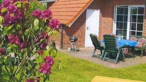 A patio area with a brick house, a barbecue grill, green chairs, and a table with a blue tablecloth. - Strandraubernest Comfortable Holiday Residence (Dornum)