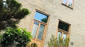 A multi-story building with a brick facade, multiple windows, and a small garden area with potted plants and a tree. - Stadthaus Emmy Marxen (Schleswig)