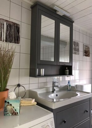 A bathroom with a white tiled wall, a dark wooden vanity, a mirror above the sink, and a potted plant on the counter. - Stadthaus Emmy Marxen (Schleswig)