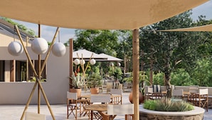 Eine Außenpatio-Terrasse mit Holztischen und -stühlen, Blumentöpfen und einem großen Sonnenschirm, der Schatten spendet.
