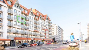 Ein mehrstöckiges Gebäude mit Balkonen, einem Fußweg und geparkten Autos.