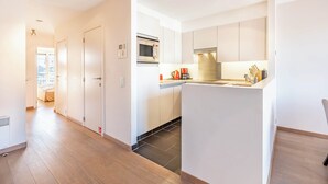 Eine moderne Küche mit weißen Schränken, einer Mikrowelle und einer Kaffeemaschine. Ein Holzboden und eine Tür zu einem anderen Raum sind vorhanden.