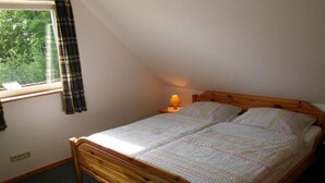 Une chambre avec un lit en bois, une fenêtre ornée de rideaux à carreaux et une lampe de chevet.