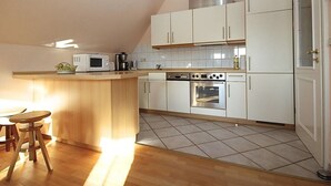Eine kompakte Küche mit Kochinsel, Mikrowelle, Kaffeemaschine und Backofen.