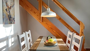 A dining area with a wooden table, white chairs, a hanging light fixture, and a painting on the wall. - Wohnung in Dargun mit Pool und Streichelzoo (Dargun)