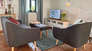A modern living room with two grey armchairs, a small coffee table, a TV on a wooden stand, a floor lamp, and a window with curtains. - Wohnung in Dargun mit Pool und Streichelzoo (Dargun)