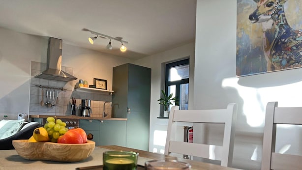 A modern kitchen with a dining area, featuring a wooden table with a fruit bowl, candles, and a green candle holder. - Wohnung in Dargun mit Pool und Streichelzoo (Dargun)