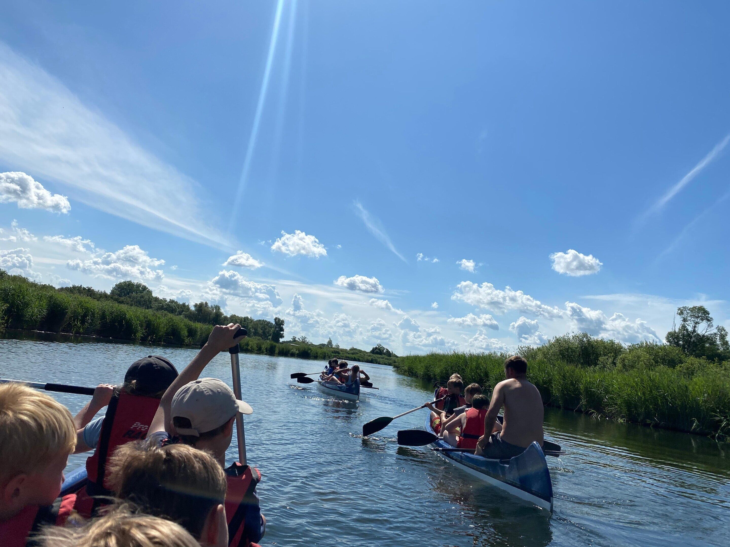 A group of people in a canoe on a river, with a clear sky and greenery in the background.
