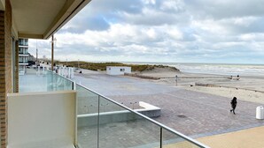 A beachside view from a balcony with a clear sky, a sandy beach, and a few people walking. - Apartment in Nieuwpoort With sea View (Nieuwpoort)