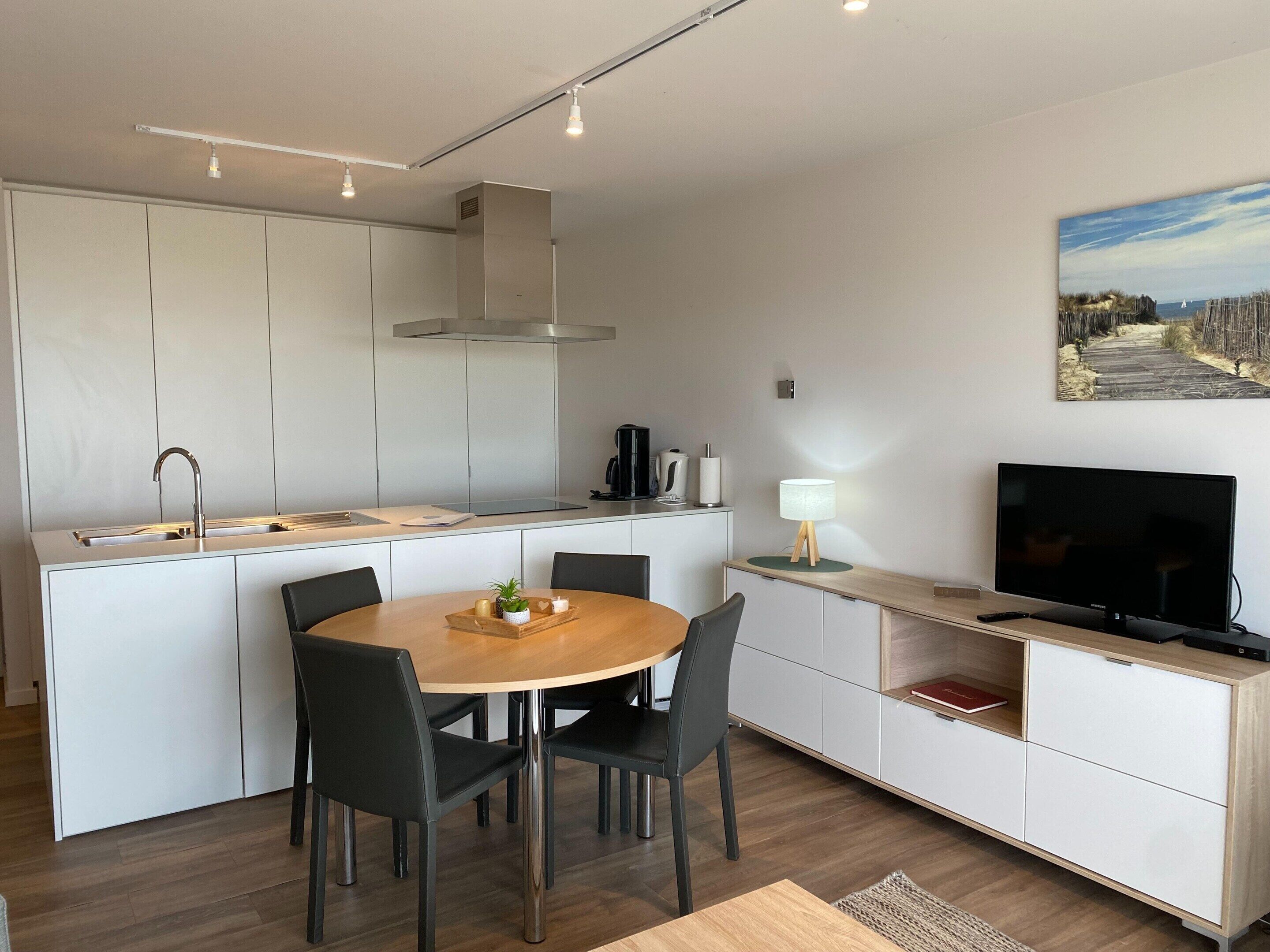 A modern kitchen with a dining area, a TV, and a painting on the wall.