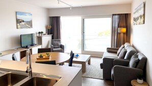 A modern living room with a sofa, a dining table, and a kitchen area with a sink and a television. - Apartment in Nieuwpoort With sea View (Nieuwpoort)