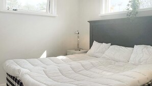 Un dormitorio con una cama, dos mesitas de noche, una lámpara y ventanas.