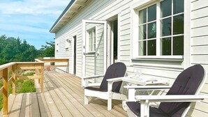 A wooden deck with outdoor furniture, including two chairs and a table, in front of a white building with large windows.