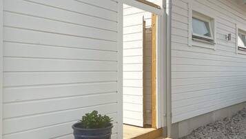 A white house exterior with a wooden door, a window, and a potted plant on the porch.