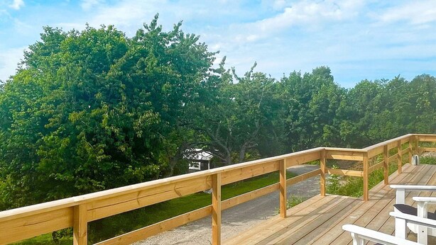 Una terraza de madera con barandilla, un banco y vistas a un área boscosa.