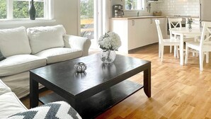 Una sala de estar moderna con una mesa de centro de madera oscura, un sofá blanco y un comedor con sillas blancas.