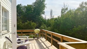 A wooden deck with a barbecue grill, outdoor seating, and a view of dense greenery.