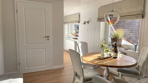 A dining area with a round wooden table, white chairs, and a hanging light fixture. - Holiday Home Reimers (Windeby)