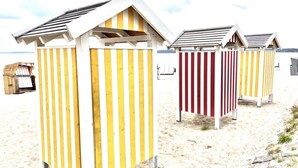 Beach huts with striped walls, a wooden structure to the left, and a sandy beach in the background. - Holiday Home Reimers (Windeby)