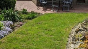 Une maison en briques avec un toit en tuiles, une terrasse avec des chaises et une table, et une pelouse bien entretenue.