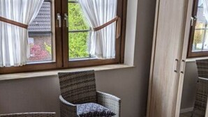 Une pièce meublée de meubles en osier, avec une table en verre et une vue sur l’extérieur, visible à travers une fenêtre ornée de rideaux.