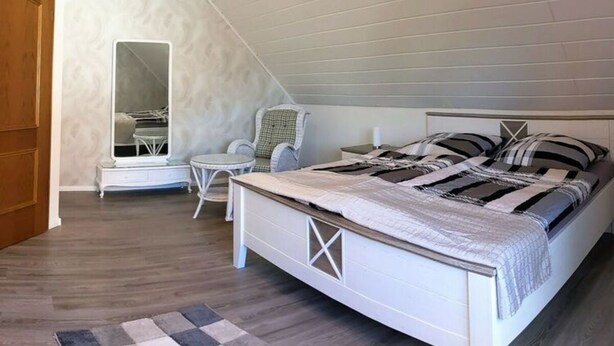 Une chambre à coucher avec un lit, une chaise, une petite table et un miroir.