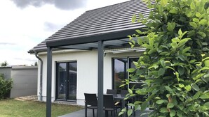 Une maison moderne dotée d’un patio couvert, d’une porte-fenêtre coulissante et d’une pelouse bien entretenue.