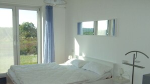 Une chambre moderne avec un grand lit, une table de chevet avec une lampe, un lampadaire et une vue sur la verdure par la fenêtre.