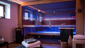 Een moderne spa-ruimte met een sauna in glazen wand, houten vloer en een bank met handdoeken.