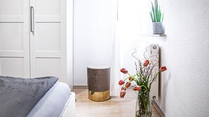 Een slaapkamer met een bed, een nachtkastje, een klein krukje, een bloempot en een radiator aan de muur.