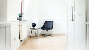 Een lichte, kleine kamer met een houten vloer, een zwarte stoel, een tafeltje met een wereldbol en een plant in een pot.
