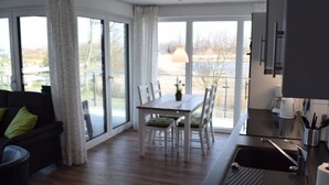 A modern kitchen with a dining area, large windows, and a view of the outdoors. - Dune View No. 3 Comfortable Vacation Home (Heiligenhafen)