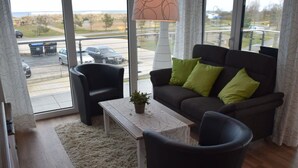 A modern living room with a sofa, two armchairs, a coffee table, and a view of a parking lot through large windows. - Dune View No. 3 Comfortable Vacation Home (Heiligenhafen)