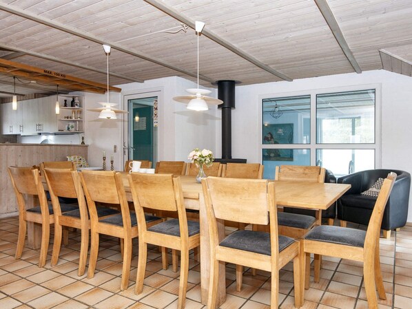 A dining area with wooden chairs and a table, a kitchen in the background, and a large window with a view.