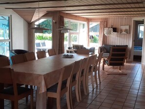 A dining area with a wooden table and chairs, large windows with curtains, and a view of the outdoors. - 4 Star Holiday Home in Nordborg (Nordborg)