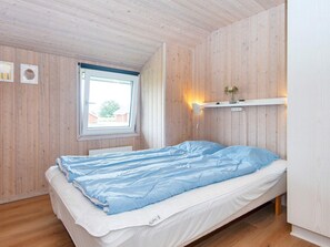 Ein Einzelbett mit einer blauen und weißen Tagesdecke, ein Fenster mit Blick ins Freie und ein an der Wand befestigtes Regal mit einer Vase.