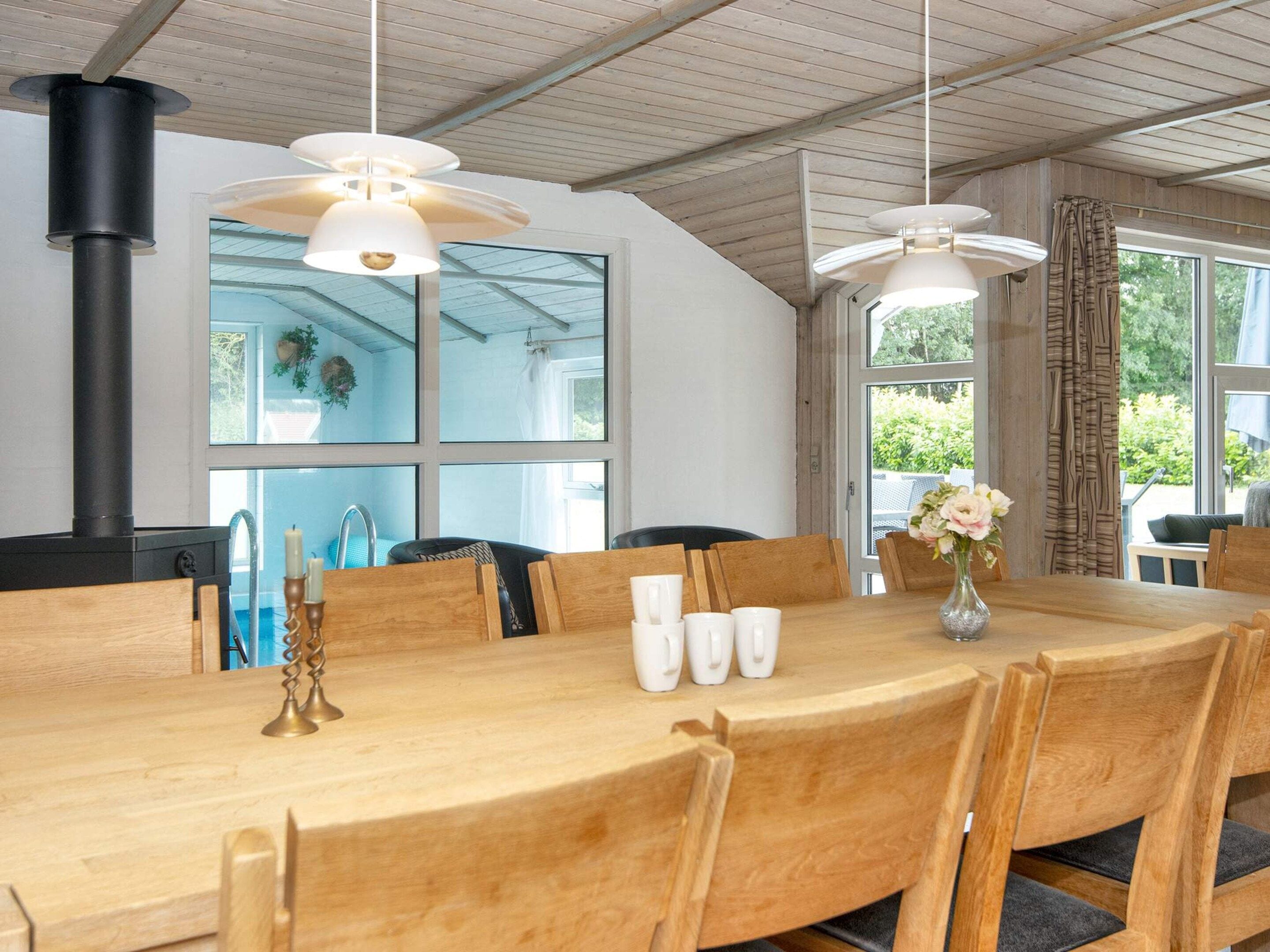 A dining area with a wooden table, chairs, hanging pendant lights, and a black stove.
