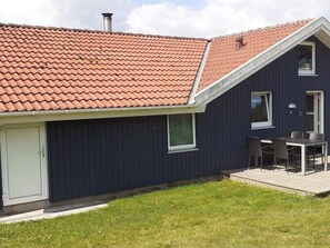 A modern house with a red-tiled roof, a dark blue exterior, and a small patio with a table and chairs. - 4 Star Holiday Home in Nordborg (Nordborg)