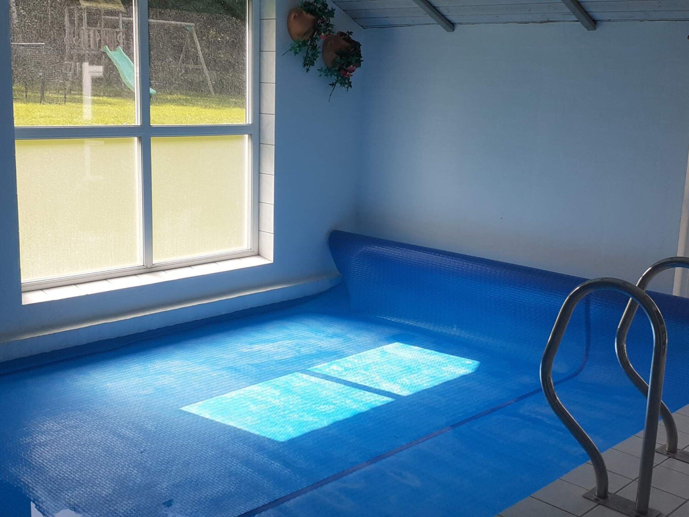 Uma piscina com chão azul, uma janela e uma escada de metal.