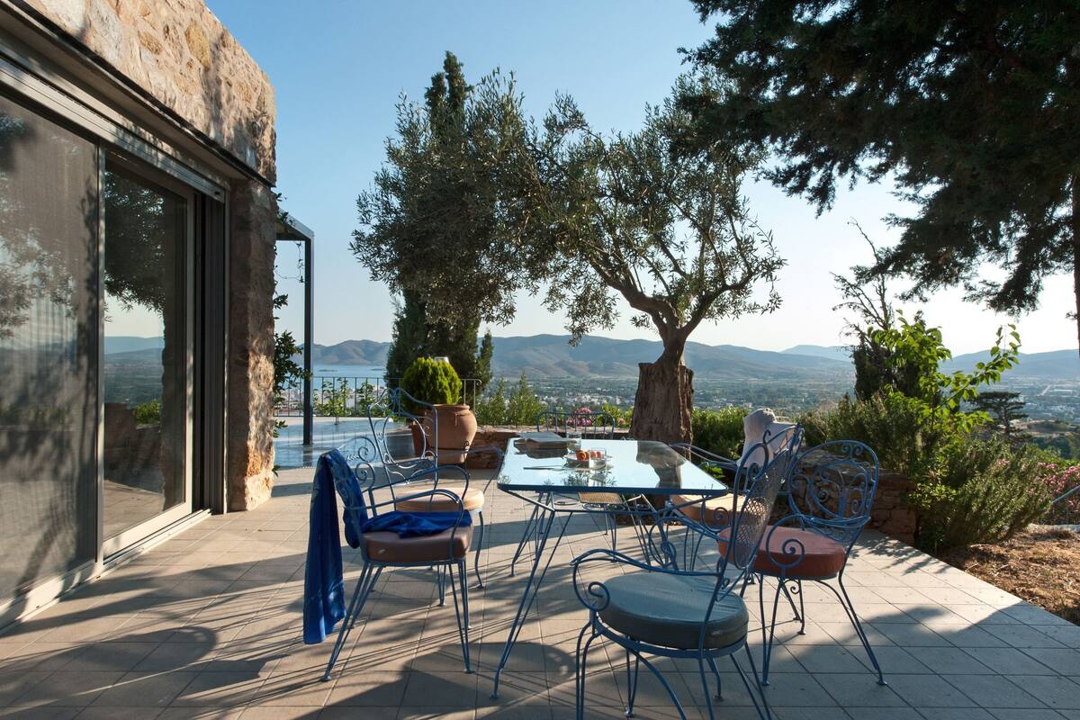 Un patio exterior con una mesa y sillas, con vista panorámica a montañas y una masa de agua.